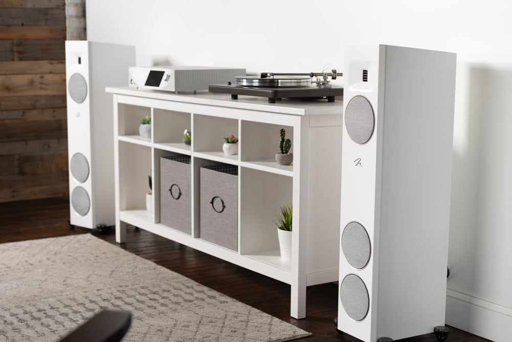Dvojica bielych stĺpových reproduktorov MartinLogan, medzi nimi skrinka s gramofónom